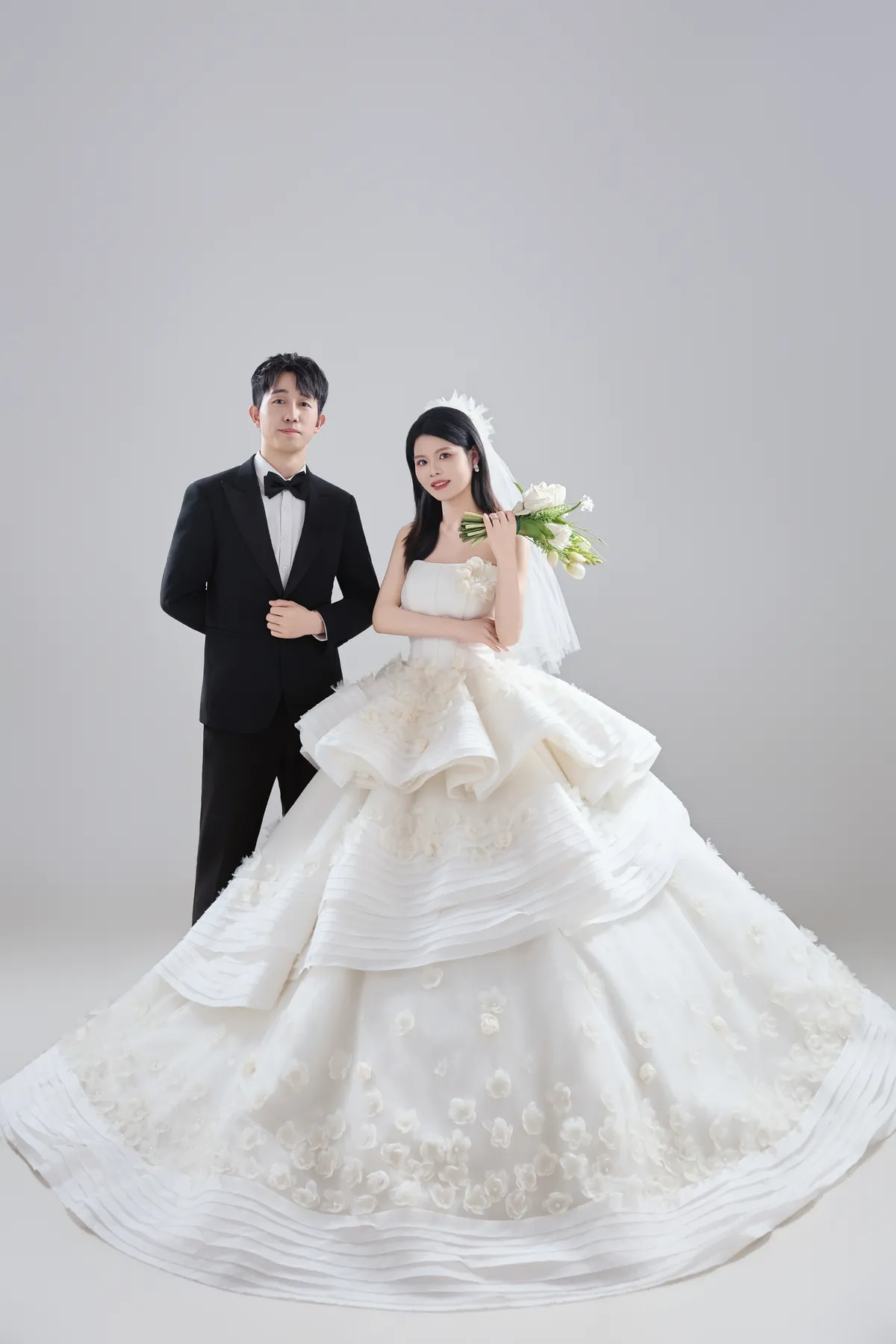 在灰色背景前携手站立的新郎与新娘